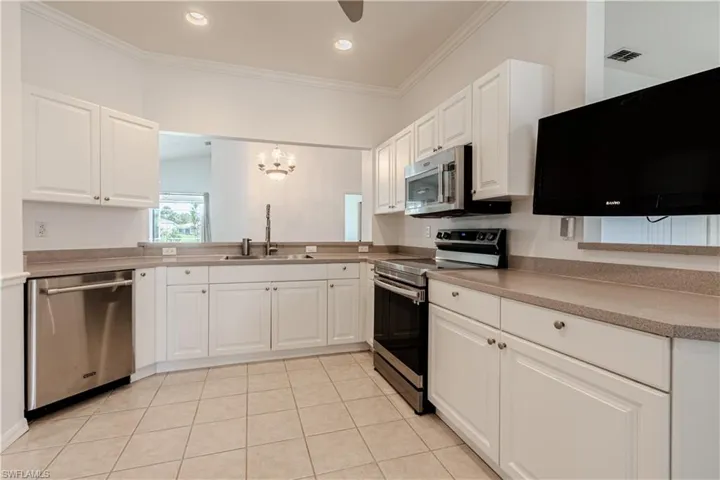 Recently painted white -Kitchen featuring light tile patterned floors, stainless steel appliances, ornamental molding, and white cabinets