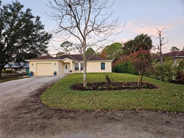 Ranch-style home featuring driveway, stucco siding, a garage, and a lawn