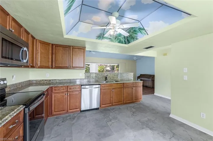 Kitchen with appliances with stainless steel finishes, sink, ceiling fan, light tile patterned floors, and a tray ceiling