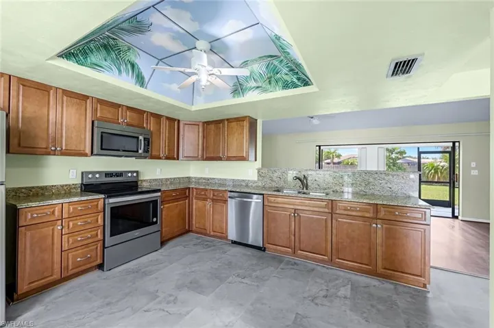 Kitchen featuring appliances with stainless steel finishes, a tray ceiling, sink, light tile patterned floors, and ceiling fan