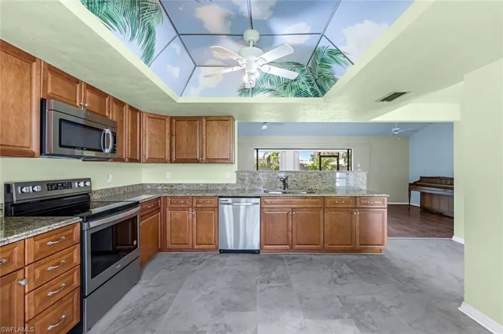 Kitchen with light tile patterned flooring, ceiling fan, light stone countertops, appliances with stainless steel finishes, and sink