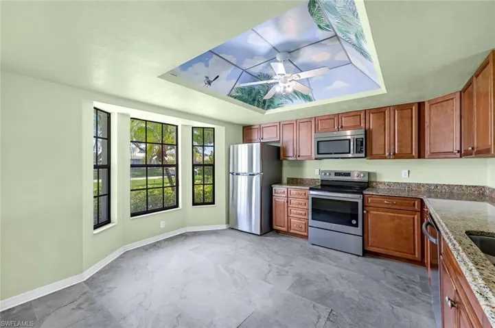 Kitchen with light tile patterned flooring, appliances with stainless steel finishes, ceiling fan, and a raised ceiling