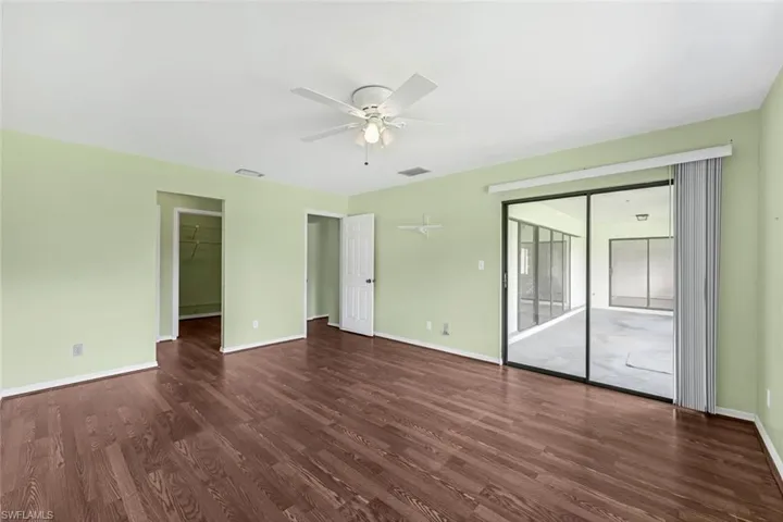 Unfurnished bedroom with dark wood-type flooring, a spacious closet, access to outside, and ceiling fan