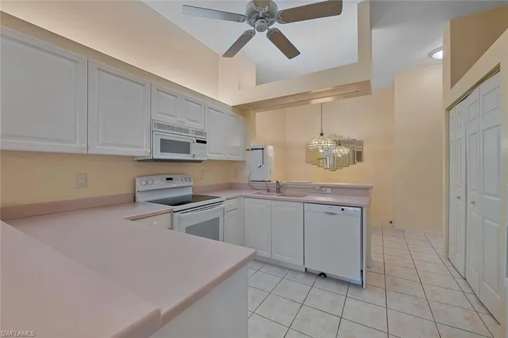 Kitchen featuring white appliances, white cabinetry, kitchen peninsula, and pink corian counters