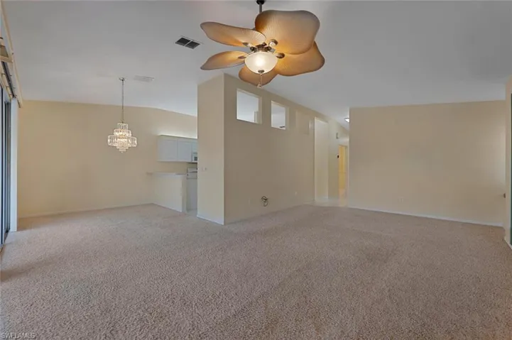 Unfurnished living room featuring vaulted ceiling, light carpet, and ceiling fan with notable chandelier
