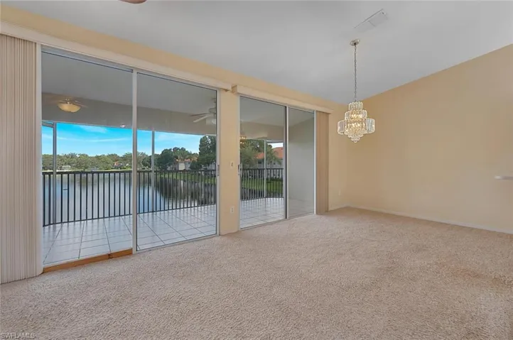 Empty room with a water view, carpet flooring, and ceiling fan with notable chandelier