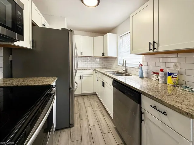 Kitchen with light stone countertops, stainless steel appliances, white cabinets, wood finish floors, and backsplash