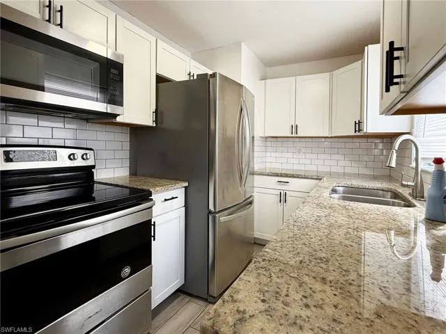Kitchen featuring appliances with stainless steel finishes, white cabinets, light stone countertops, and decorative backsplash