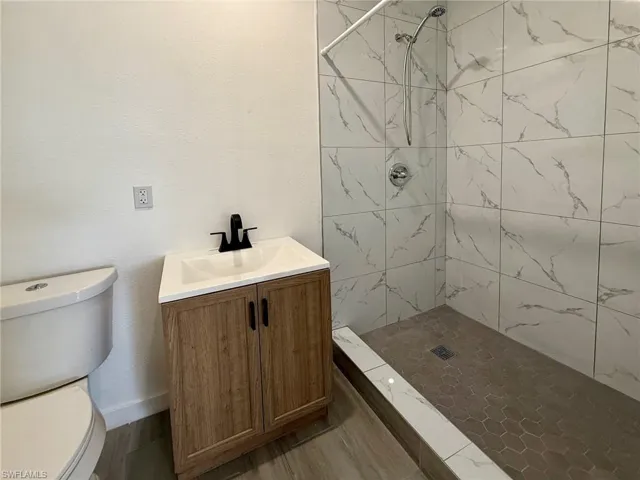 Guest bathroom featuring a shower stall, vanity, a textured wall, and dark wood finished floors