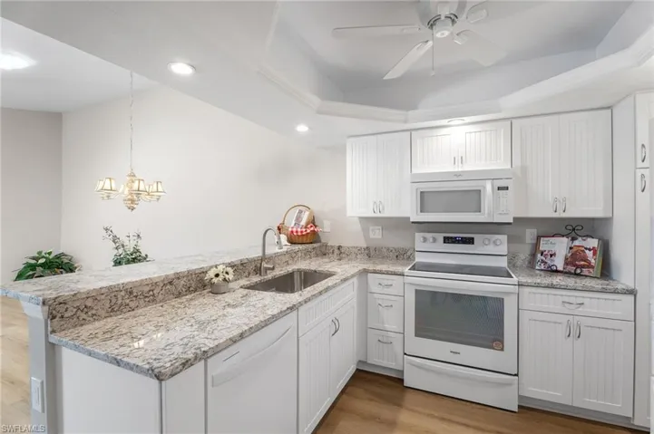 Kitchen featuring granite countertops, a tray ceiling, light wood finished floors microwave and stove.