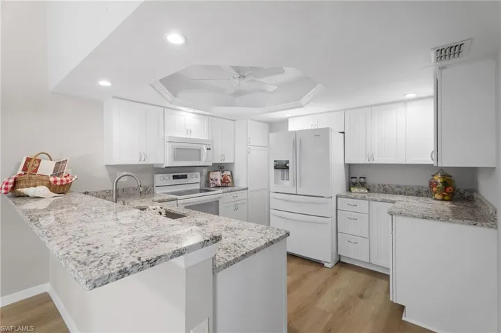 Kitchen featuring granite countertops, white appliances, a peninsula, and a raised ceiling.