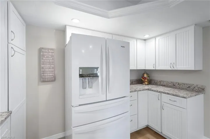 Kitchen with white cabinets, upgraded white refrigerator with ice dispenser, and light granite stone counters.