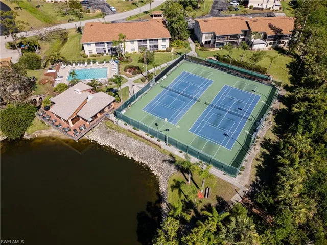 Aerial view of clubhouse, tennis/pickleball courts, pool and lake.