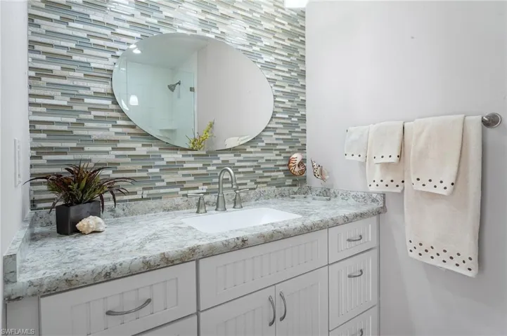 Primary bathroom featuring tiled shower, vanity, and decorative backsplash.