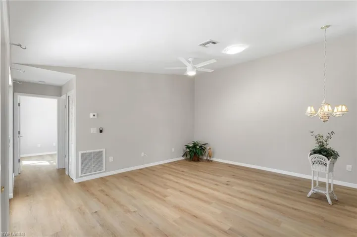 Unfurnished room featuring ceiling fan, skylight, custom chandelier, baseboards, and light wood-style flooring.