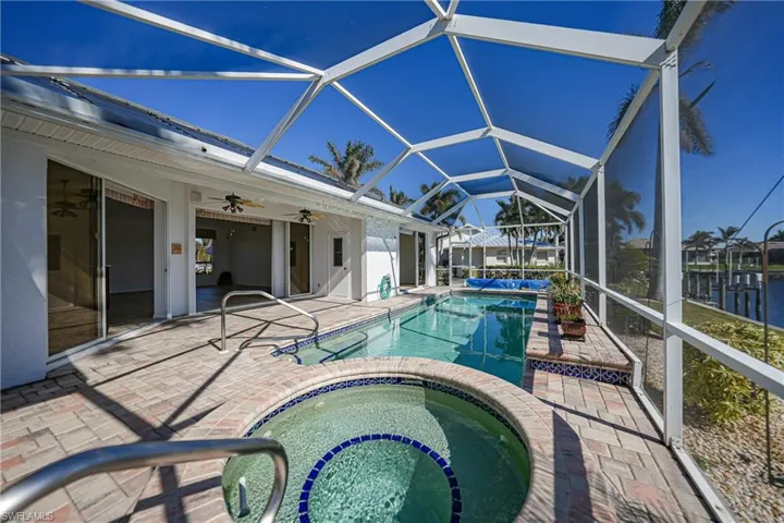 View of swimming pool featuring a lanai, an in ground hot tub, a water view, and a patio