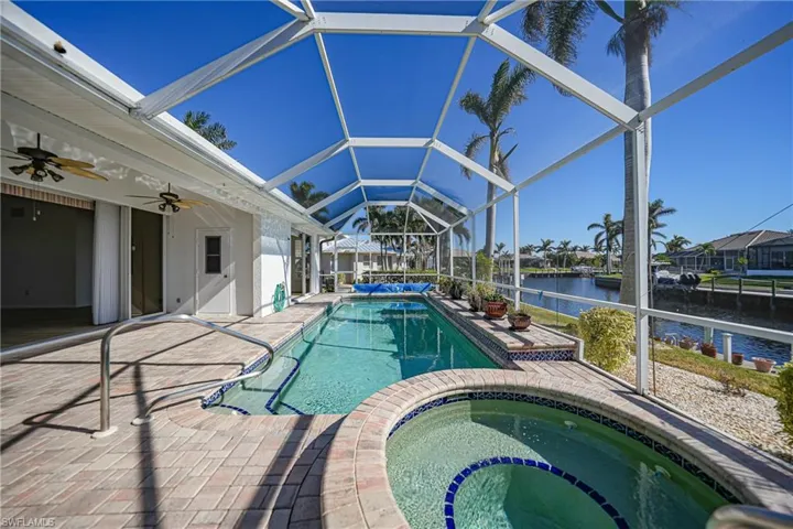View of pool with an in ground hot tub, a water view, a patio area, and a lanai