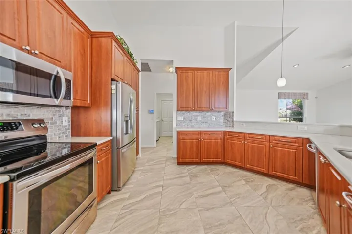 Kitchen featuring decorative light fixtures, backsplash, stainless steel appliances, and vaulted ceiling