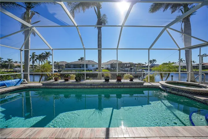 View of swimming pool featuring an in ground hot tub, a water view, and glass enclosure