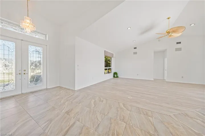 Unfurnished living room with french doors, a healthy amount of sunlight, ceiling fan with notable chandelier, and light hardwood / wood-style floors