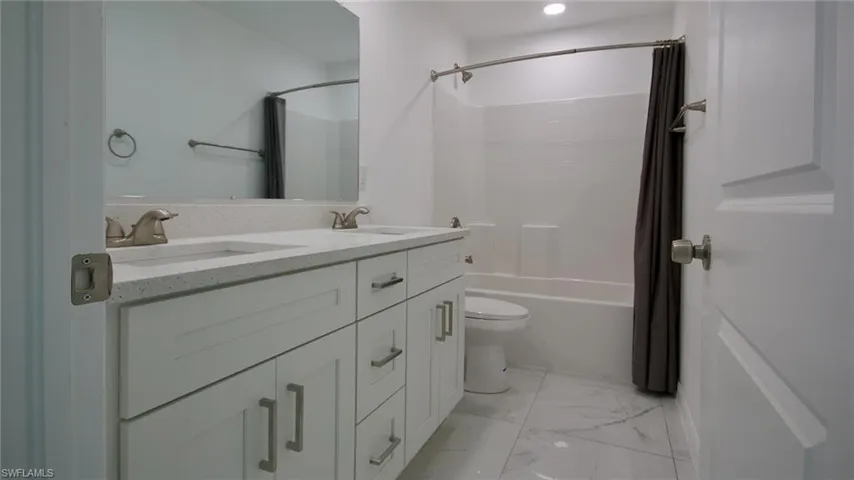 Bathroom with marble finish floor, double vanity, toilet, and a sink