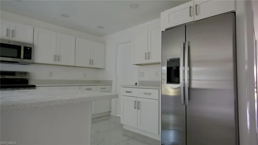 Kitchen with marble finish floor, white cabinets, light stone counters, and appliances with stainless steel finishes