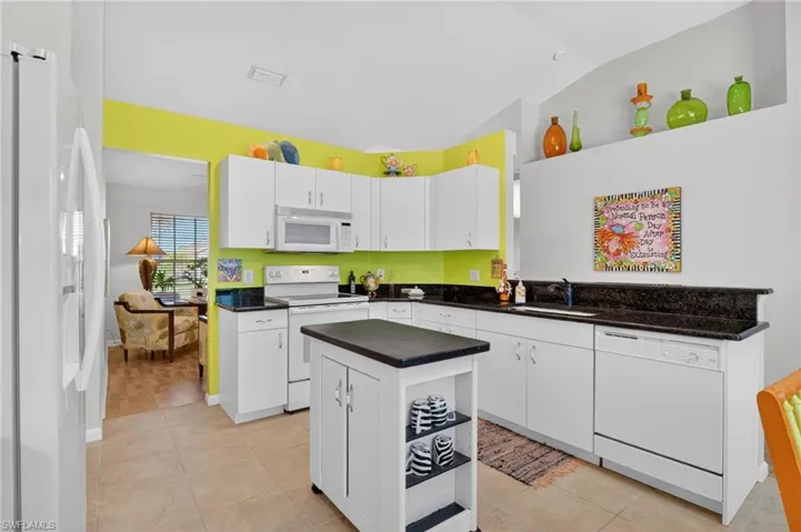 Kitchen with white appliances, white cabinetry, light tile patterned flooring, lofted ceiling, and a kitchen island