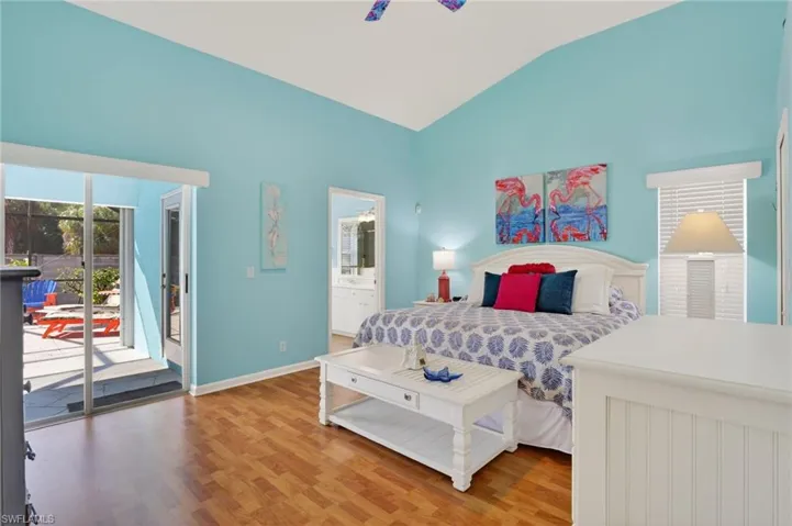 Bedroom featuring access to exterior, light wood-style flooring, vaulted ceiling, connected bathroom, and a ceiling fan