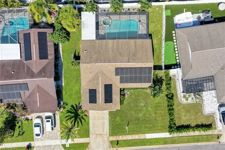 Aerial perspective featuring a residential property with a screened-in pool and spa, rooftop solar panel array, and a concrete driveway