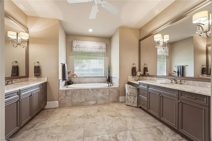 Full bath featuring healthy amount of natural light, two vanities, a garden tub, and a chandelier