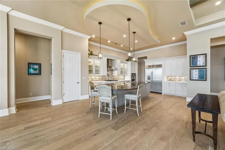 Kitchen with pendant lighting, backsplash, a kitchen bar, white cabinets, and ornamental molding