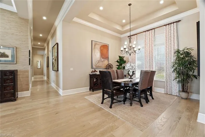 Dining area featuring light wood finished floors, crown molding, a chandelier, recessed lighting, and a raised ceiling