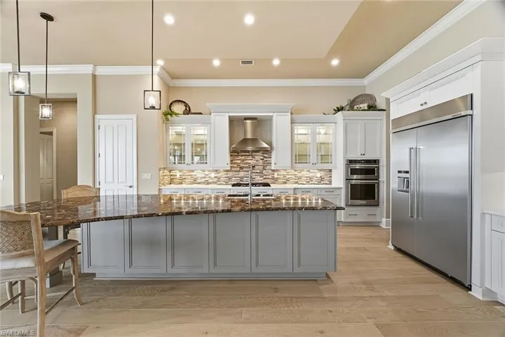 Kitchen featuring glass insert cabinets, stainless steel appliances, dark stone countertops, white cabinetry, and hanging light fixtures