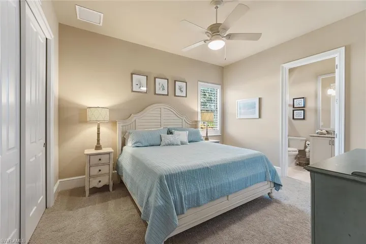 Bedroom with a closet, light colored carpet, ceiling fan, and ensuite bath