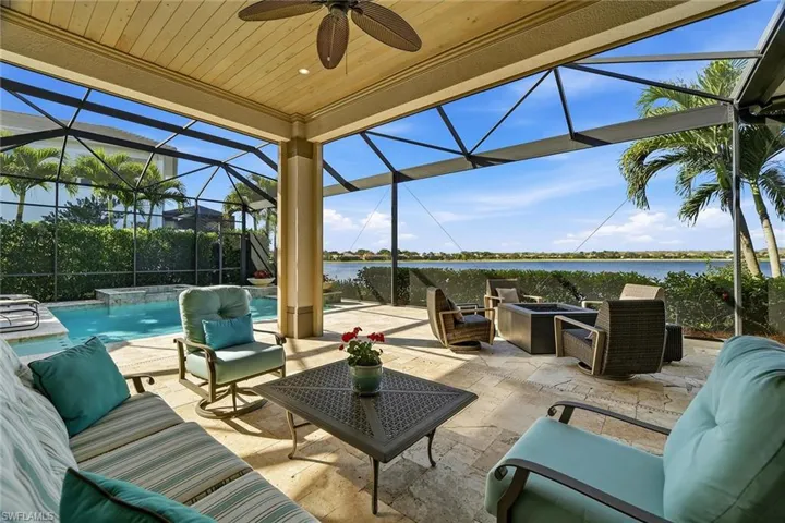 View of patio featuring glass enclosure, an outdoor living space with a fire pit, a water view, ceiling fan, and a sunroom