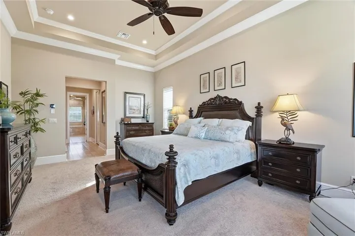 Bedroom with multiple windows, ceiling fan, light carpet, a tray ceiling, and crown molding
