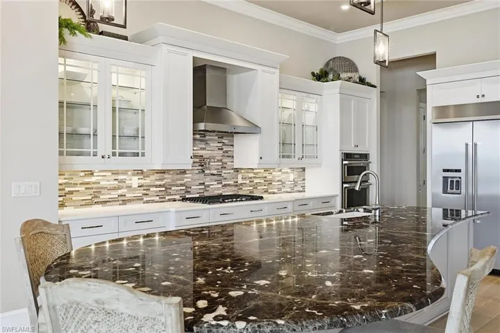 Kitchen featuring hanging light fixtures, dark stone countertops, appliances with stainless steel finishes, wall chimney exhaust hood, and ornamental molding