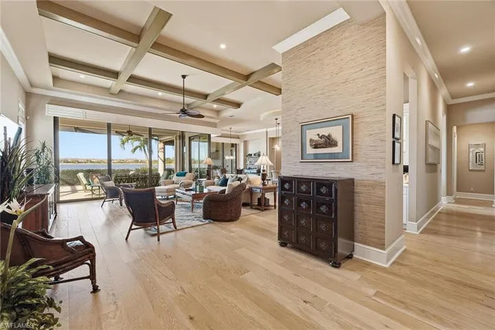 Living room with ceiling fan, a water view, light wood-style flooring, coffered ceiling, and crown molding
