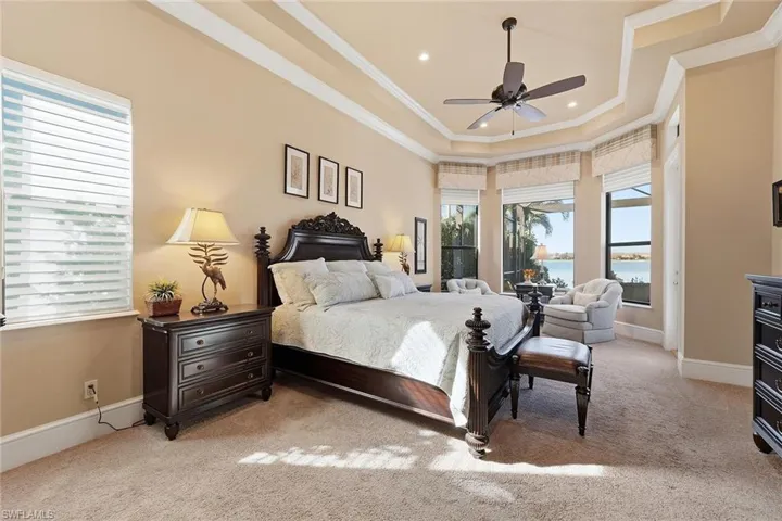 Bedroom with a water view, light carpet, a tray ceiling, ornamental molding, and ceiling fan