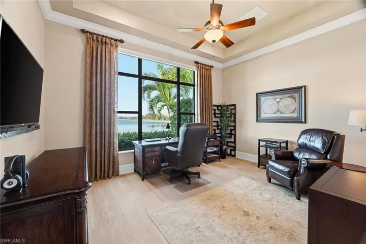Office featuring a water view, a raised ceiling, light wood-type flooring, ornamental molding, and ceiling fan