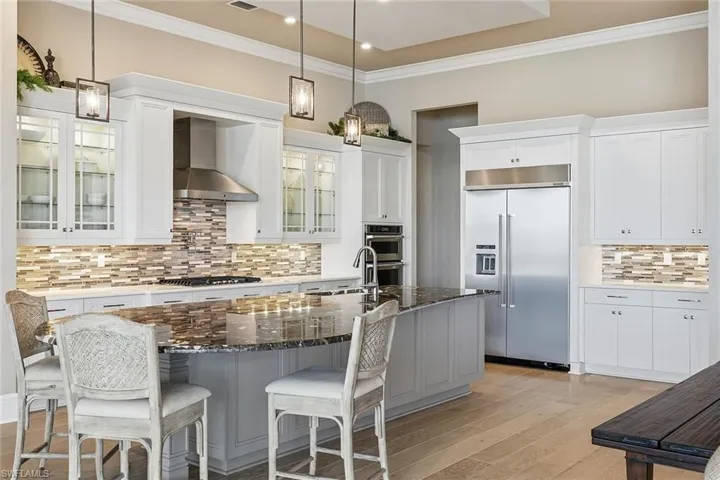Kitchen with dark stone counters, appliances with stainless steel finishes, a kitchen island with sink, wall chimney range hood, and crown molding