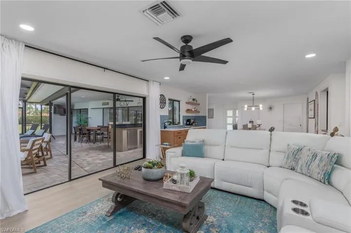 Living room featuring light wood-type flooring, a wealth of natural light, visible vents, and ceiling fan with notable chandelier