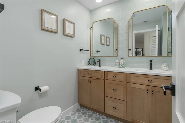 Bathroom featuring toilet, a sink, baseboards, decorative backsplash, and double vanity