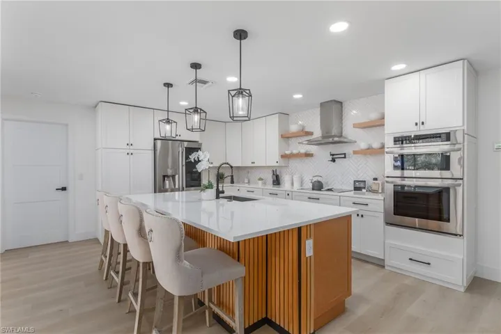 Kitchen with visible vents, wall chimney exhaust hood, appliances with stainless steel finishes, a sink, and open shelves