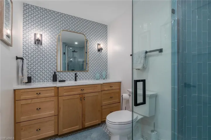 Bathroom featuring vanity, toilet, a shower stall, and wallpapered walls
