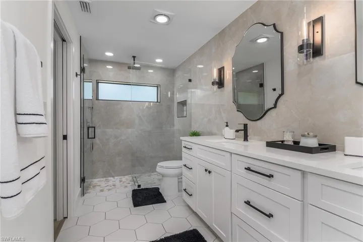Full bathroom featuring tile walls, toilet, a sink, a stall shower, and visible vents