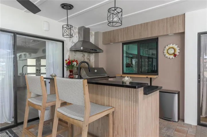 Kitchen featuring fridge, stone finish floor, hanging light fixtures, dark countertops, and wall chimney range hood