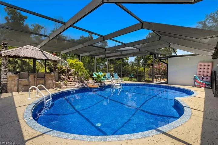 Tropical beach vibes outback with the waterfall and concrete pool deck designed to look like a sandy beach.
