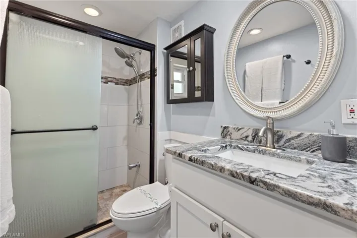 Primary bathroom with glass shower door, new vanity with granite top, and tiles shower.