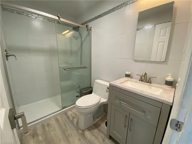 Bathroom with tile walls, a stall shower, vanity, and light wood-type flooring